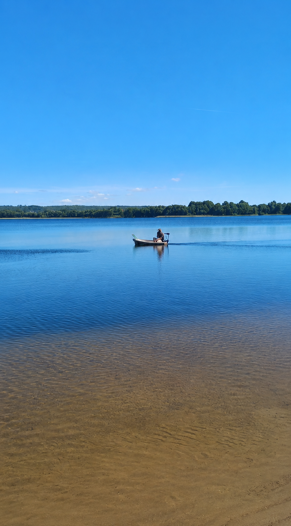 Spokojna plaża nad jeziorem Raduńskim — łódka na lustrze wody